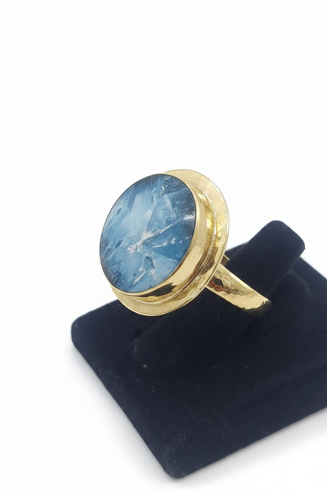 Gold ring with a blue stone on a black stand against a white background