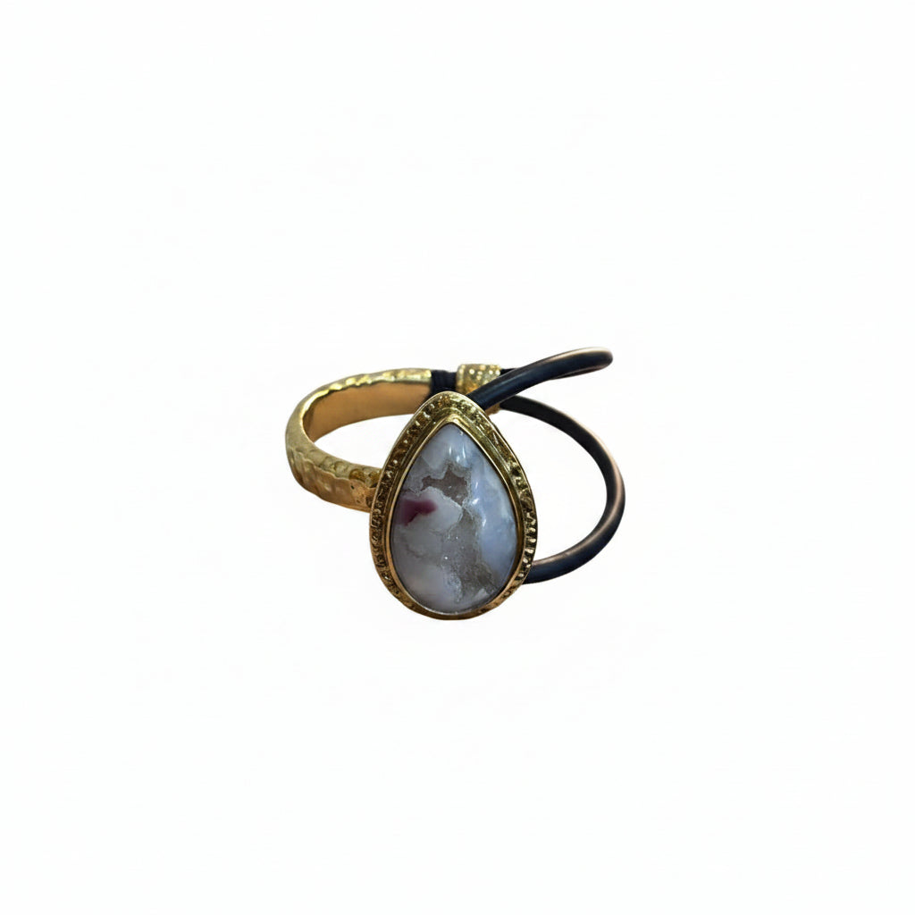 Hand holding a gold bracelet with a stone and black hair tie against a light background