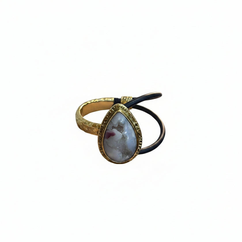 Hand holding a gold bracelet with a stone and black hair tie against a light background