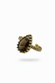 Gold ring with a large brown gemstone held in a hand, with a laptop in the background.