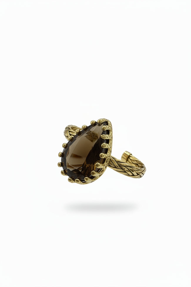 Gold ring with a large brown gemstone held in a hand, with a laptop in the background.