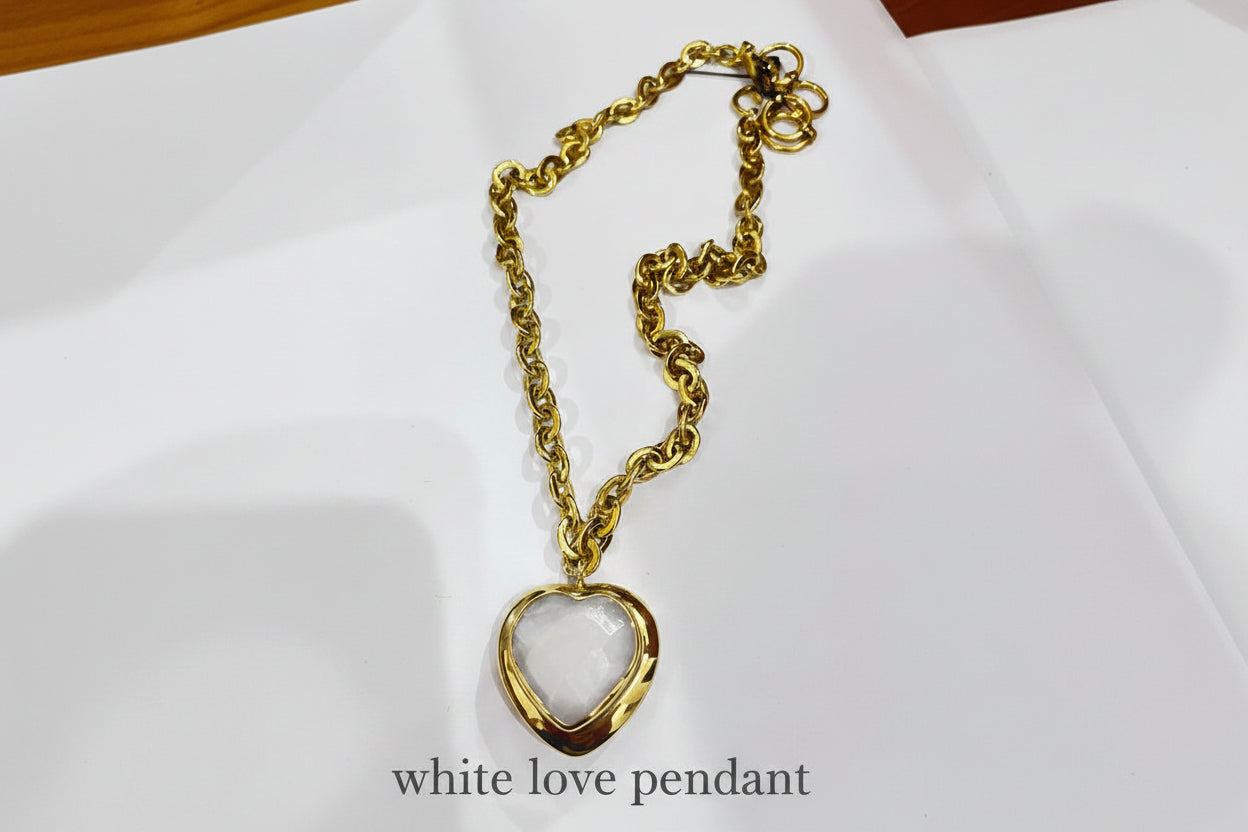 Gold chain necklace with a heart-shaped white pendant on a white background