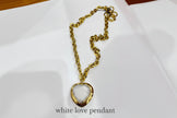 Gold chain necklace with a heart-shaped white pendant on a white background
