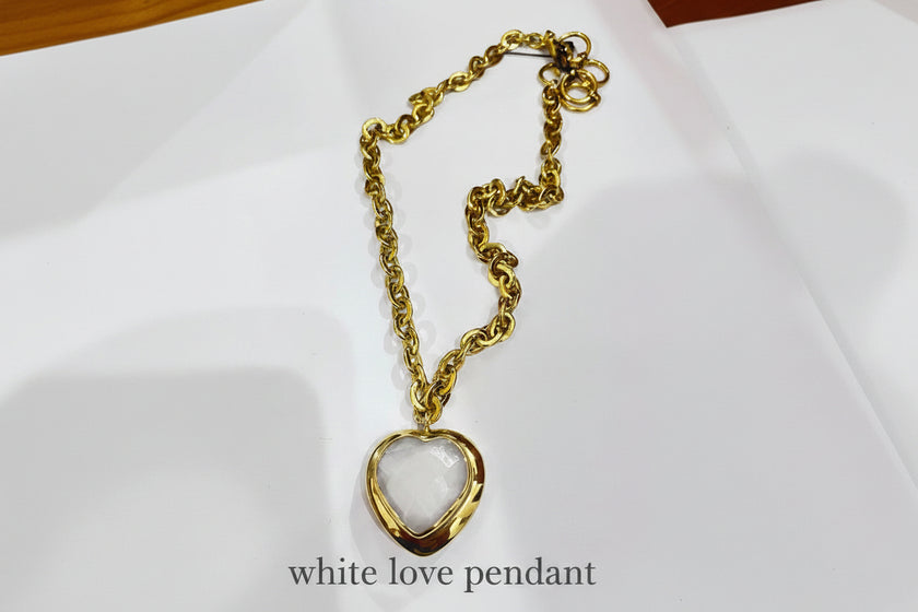 Gold chain necklace with a heart-shaped white pendant on a white background