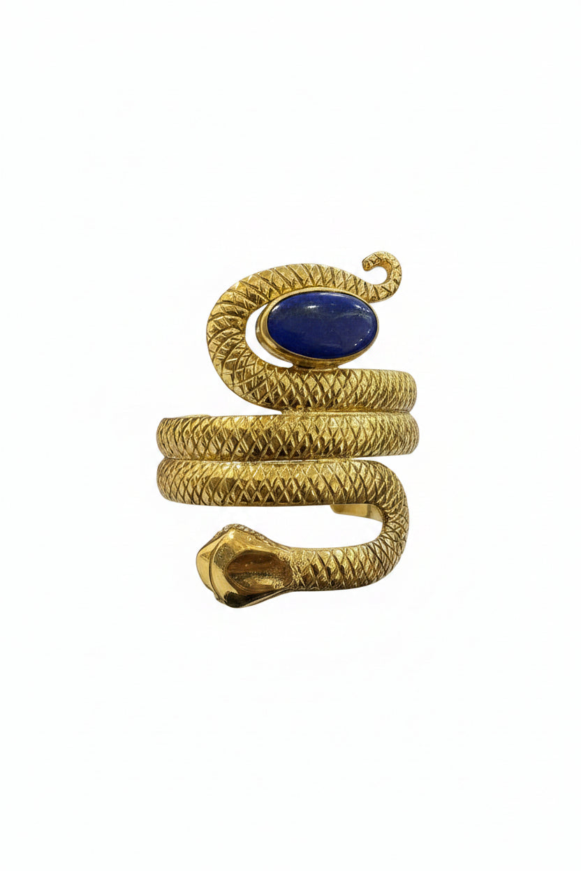 Gold snake-shaped bracelet with a blue stone held in front of a laptop on a desk.